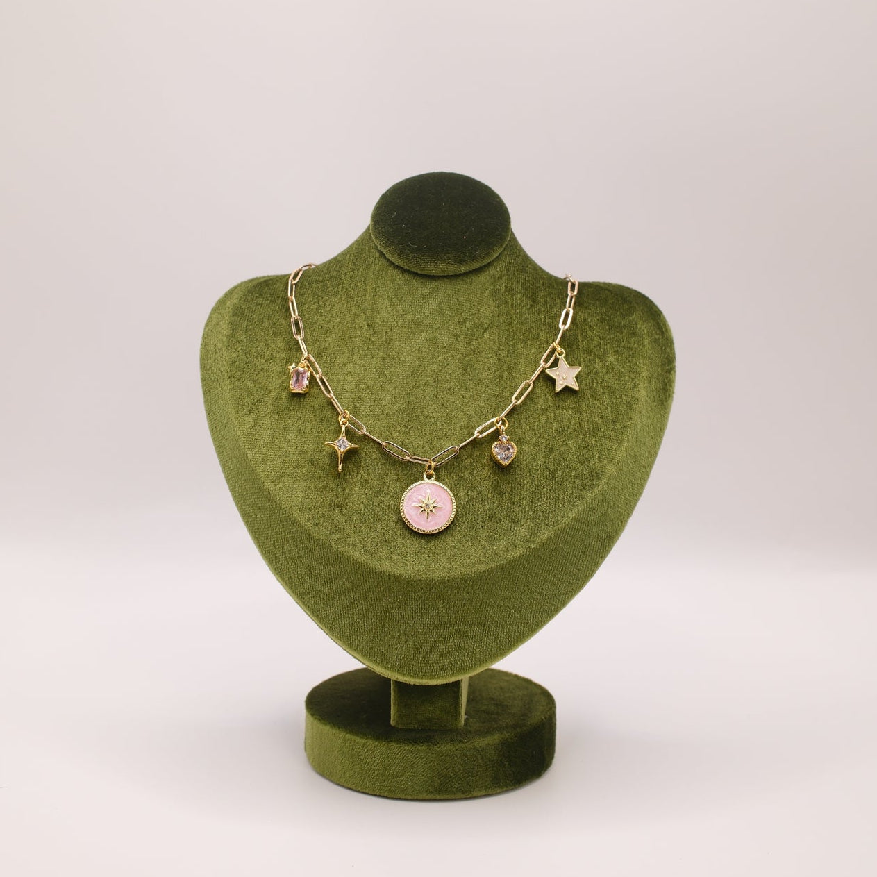 Gold necklace with charms on a green velvet jewelry stand against a white background