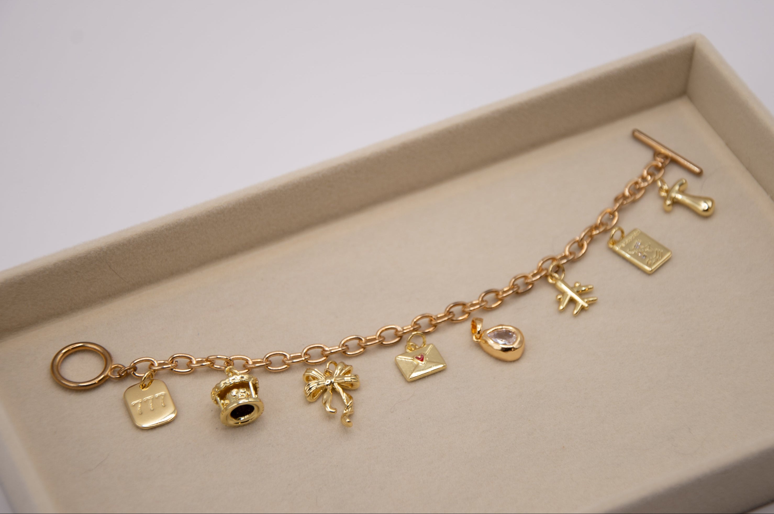Gold charm bracelet on a beige tray with a white background