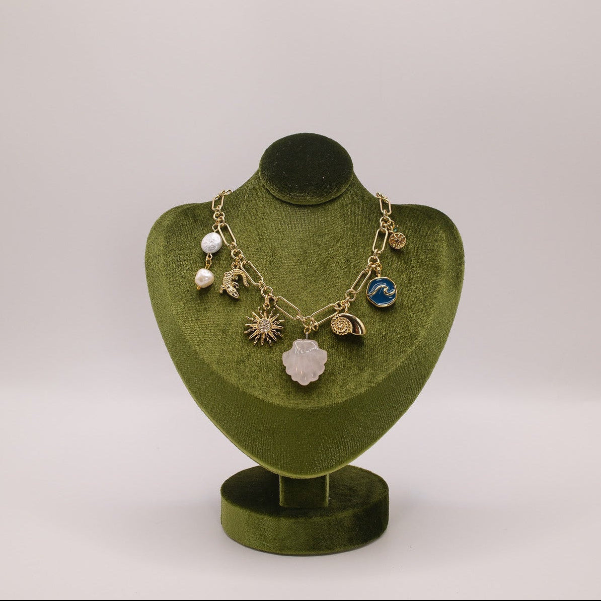 Necklace with various charms on a green velvet stand against a light gray background