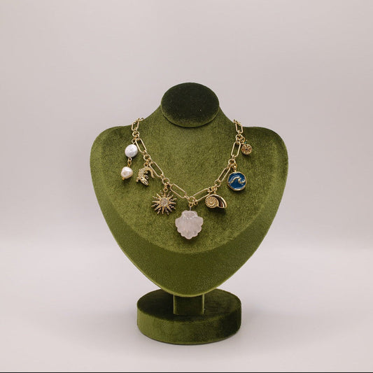 Necklace with various charms on a green velvet stand against a light gray background